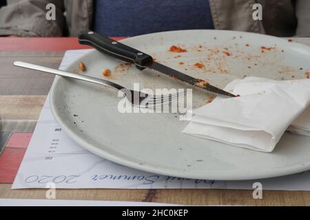 Piatto bianco vuoto con pangrattato di pizza. Sul piatto poco profondo è posate come coltello, forchetta e tovagliolo. Una scena da un ristorante. Foto Stock