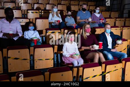 Adulti con bambini in maschere protettive guardando film al cinema Foto Stock