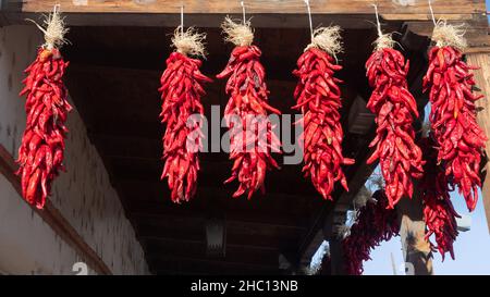 Più mazzi di Chile Pepper Ristras appesi da una trave di legno nella città vecchia Albuquerque fuori al sole. Foto Stock