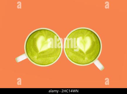 Coppia di tè verde Matcha con latte Art a forma di cuore isolato su sfondo arancione Foto Stock