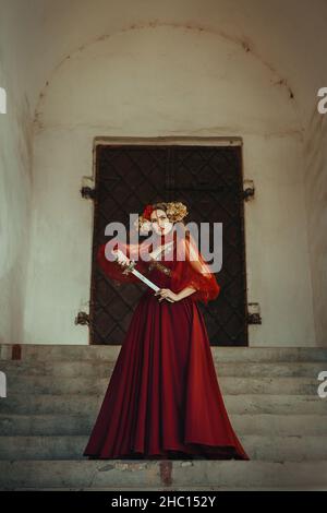 La giovane guerriera sta posando con un coltello che indossa un abito rosso Foto Stock