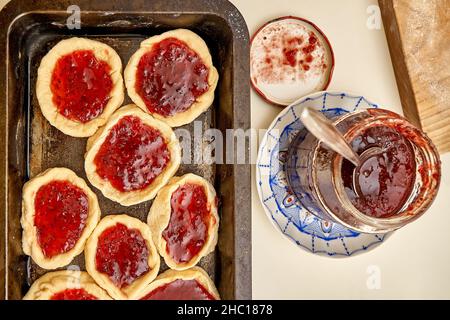 Torte aperte crude riempite con deliziosa marmellata fatta in casa di ribes in grande piatto da forno su tavola bianca in cucina vista ravvicinata superiore Foto Stock