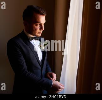 giovane uomo in camicia bianca che fissa i gemelli sulle maniche vicino alla finestra. ritratto aziendale. Lo sposo incontrerà la sposa. Matrimonio, uomo d'affari Foto Stock