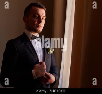 giovane uomo in camicia bianca che fissa i gemelli sulle maniche vicino alla finestra. ritratto aziendale. Lo sposo incontrerà la sposa. Matrimonio, uomo d'affari Foto Stock