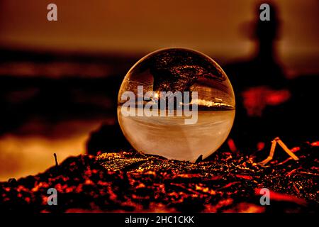 Rappresentazione astratta di una sfera di vetro su un groyne sul Mar Baltico. L'ambiente sembra bruciarsi. Sembra che la sfera di vetro si trovi sul bruciare la Foto Stock