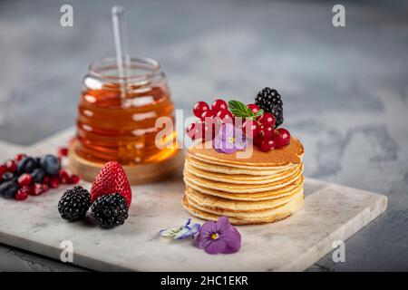 Pancake. Sana colazione estiva, frittelle classiche americane fatte in casa con bacche fresche e miele, mattina grigio chiaro pietra sfondo copia spazio top v Foto Stock