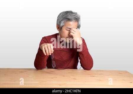 L'uomo asiatico anziano seduto al banco su sfondo bianco. Foto Stock