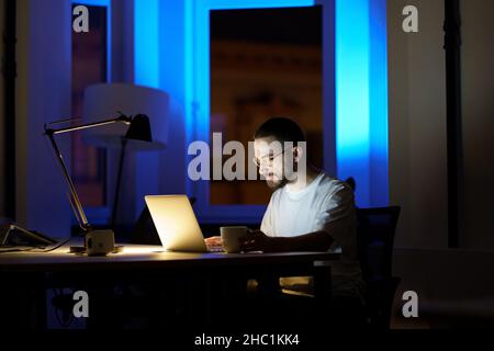 Il giovane uomo d'affari premuroso in occhiali lavora sul laptop di notte preparandosi per la presentazione iniziale Foto Stock