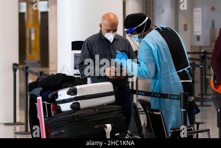 (211221) -- MISSISSAUGA (CANADA), 21 dicembre 2021 (Xinhua) -- Un operatore medico che indossa dispositivi di protezione personale aiuta un viaggiatore internazionale all'aeroporto internazionale Pearson di Toronto a Mississauga, Ontario, Canada, il 21 dicembre 2021. Il Canada ha segnalato 9.597 nuovi casi COVID-19 martedì pomeriggio, portando il totale cumulativo a 1.907.180 casi con 30.082 morti, secondo CTV. (Foto di Zou Zheng/Xinhua) Foto Stock