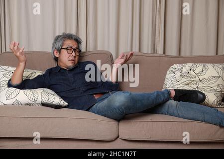 L'uomo asiatico anziano seduto sul divano in salotto. Foto Stock