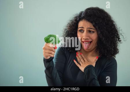 Ritratto di una giovane donna infelice con broccoli che si stacca la lingua Foto Stock