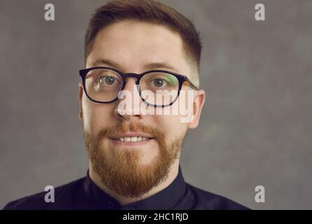 Primo piano del volto di un fiducioso giovane uomo d'affari caucasico su sfondo grigio. Foto Stock