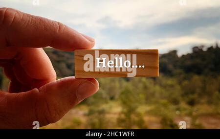 Immagine con testo Hello su un blocco di legno con una mano che tiene con e sfocato sfondo natura Foto Stock