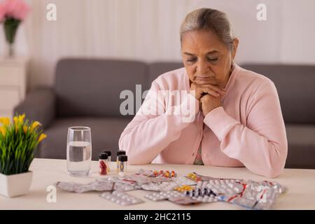Donna anziana che sta per prendere la medicina tenuta sul tavolo centrale Foto Stock