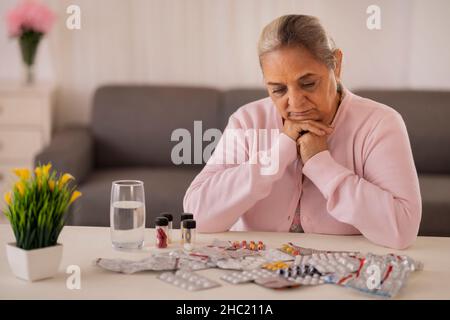 Donna anziana che sta per prendere la medicina tenuta sul tavolo centrale Foto Stock