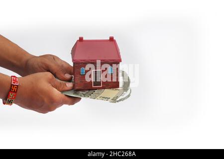Primo piano di mani dando modello di casa con banconote in valuta indiana. Concetto di casa, immobiliare e affare isolato su sfondo bianco Foto Stock