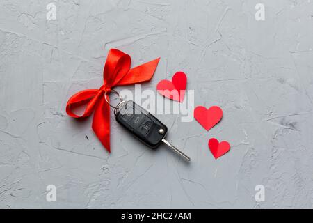 Chiave auto con arco rosso e un cuore su un tavolo colorato. Regalo o regalo per San Valentino o natale, vista dall'alto con spazio per le copie. Foto Stock