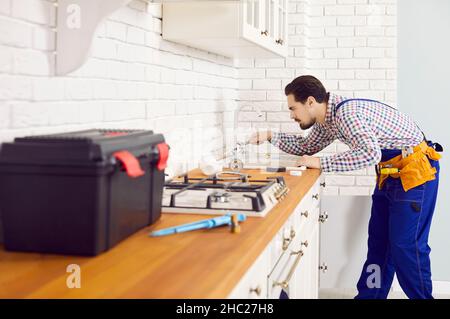 Idraulico giovane usando i suoi attrezzi per risolvere il problema del rubinetto che perde nella cucina Foto Stock