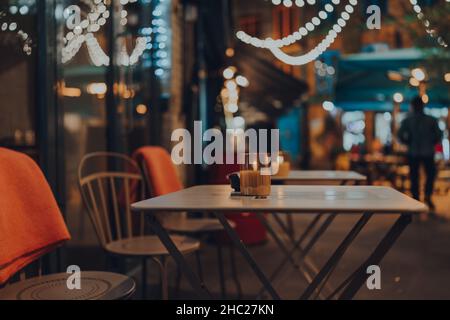 Candela illuminata a un tavolo esterno di un ristorante in inverno, luci di Natale sullo sfondo, fuoco selettivo, bokeh. Foto Stock
