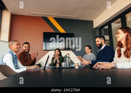 Uomini d'affari di successo applaudono il loro collega in una sala riunioni. Gruppo di uomini d'affari multietnici che si aggrappano felicemente durante la loro briefing mattutino Foto Stock