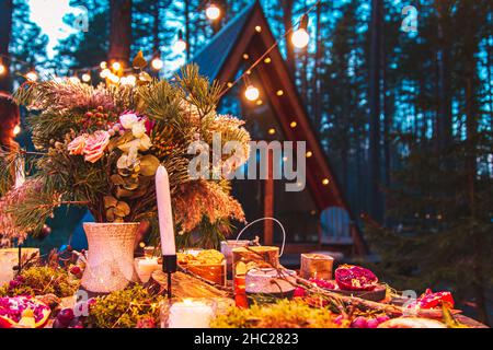 Tavolo per una cerimonia di nozze in stile ecologico nella foresta. Decorazione con fiori freschi, candele, muschio, ghirlande. Sullo sfondo c'è un blu Foto Stock