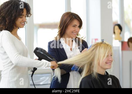 parrucchiere apprendista stiratura dei capelli dei clienti Foto Stock