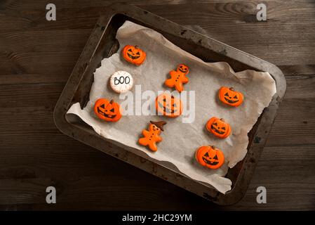 Biscotti arancioni brillanti sotto forma di zucche e uomini divertenti si trovano in una teglia da forno. Deliziosi biscotti allo zenzero arancione. Halloween. Festeggia Foto Stock