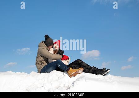 La coppia felice in amore si siede sulla neve e abbracciando. Cielo blu sullo sfondo. Foto Stock