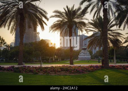 Vicolo con prato verde e alberi nel parco Zabeel, Dubai, Emirati Arabi Uniti. Vista del moderno skyline di Dubai dall'autostrada di avvicinamento al Palazzo Zabeel, Dubai, Emirati Arabi Uniti Foto Stock