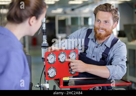 ingegnere che aiuta l'apprendista femminile in fabbrica Foto Stock