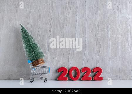Albero di Natale in miniatura in carrello sullo sfondo dell'iscrizione 2022. Acquisto e affitto di alberi di Natale. Foto Stock