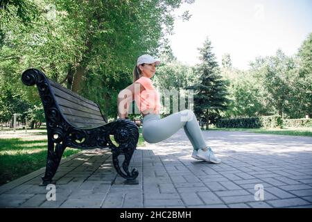 ritratto di giovane donna sportiva in parco in abbigliamento sportivo riscaldamento esercizio stretching facendo push-up dalla panca Foto Stock