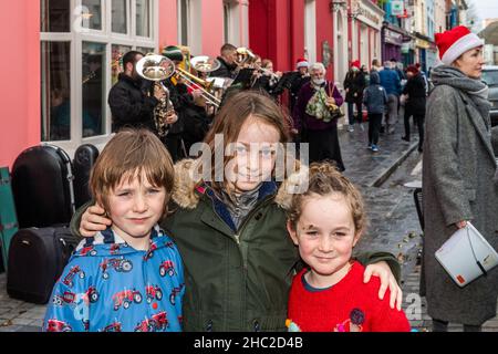 Clonakilty, West Cork, Irlanda. 23rd Dic 2021. La Clonakilty Brass Band ha giocato i caroli di Natale su Clonakilty Main Street oggi, il giorno prima della vigilia di Natale, che ha tirato una grande folla di spettatori. Guardando la band sono stati Tóla, nell e Iarlaith Horan da Clonakilty. Credit: AG News/Alamy Live News Foto Stock