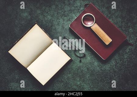 Vecchi libri, occhiali e una lente d'ingrandimento con manico in pelle, scuro e moody, vista dall'alto Foto Stock