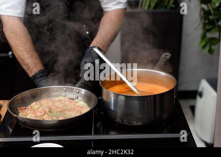 Processo di cottura della zuppa Suquet de Peix con patate, erbe e pesce con l'aggiunta di picada primo piano in una pentola sul tavolo. Foto Stock