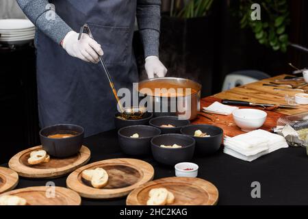 Processo di cottura della zuppa Suquet de Peix con patate, erbe e pesce con l'aggiunta di picada primo piano in una pentola sul tavolo. Foto Stock