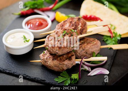 Appetitosi kebab kofta (polpette di carne) con la salsa e tortillas tacos su sfondo nero Foto Stock