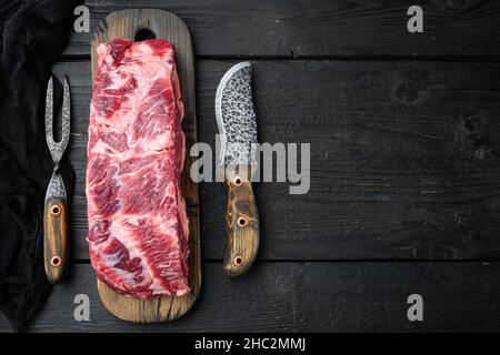 Costola cruda occhio manzo bistecca di carne marmorizzata intero taglio set, su sfondo nero tavolo di legno, vista dall'alto piatto, con spazio copia per il testo Foto Stock