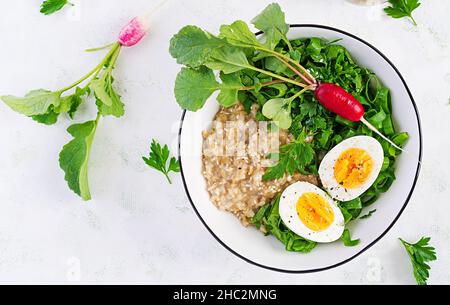 Prima colazione porridge di farinata d'avena con uova sode, rafano ed erbe verdi. Cibo sano ed equilibrato. Vista dall'alto, sopra Foto Stock