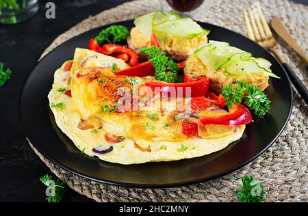 Colazione. Omelette con paprika, formaggio e pomodori con sandwich su piatto nero. Frittata - frittata italiana. Foto Stock