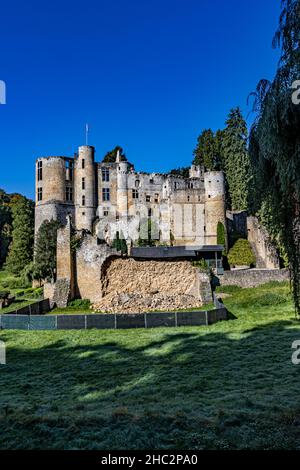 Campo con erba verde con le rovine del castello Burg Beaufort su una collina rocciosa sullo sfondo, torri, muri in pietra distrutti, soleggiata giornata estiva con Foto Stock