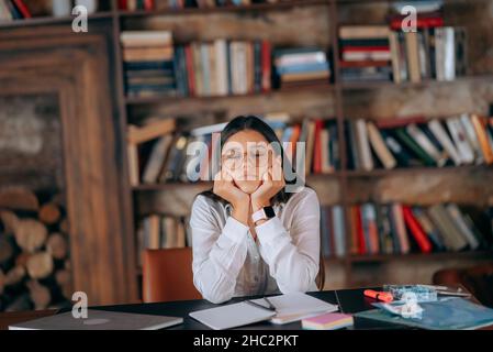 Giovane donna in ufficio che pensa al problema sullo sfondo delle librerie Foto Stock