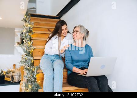 Madre e figlia seduti sui gradini e guardando qualcosa sul portatile Foto Stock