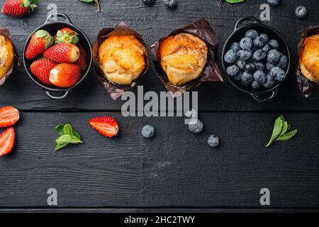 Muffin ai mirtilli con berrie fresca, su sfondo di legno nero, vista dall'alto in piano con spazio per la copia del testo Foto Stock