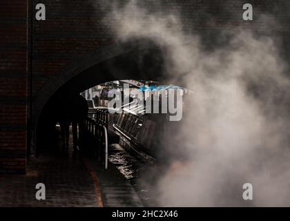Canal River Boat passando sotto il vecchio ponte ad arco con fumo atmosferico motore da motore diesel stretto barca motore chiatta motore. Foto Stock