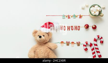 Decorazioni natalizie su sfondo bianco. Orsacchiotto di Natale con cappello di Santa, tazza di cacao e caramelle, spazio copia Foto Stock