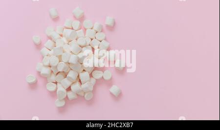 Marshmallow su sfondo rosa pastello, spazio di copia. Mini dessert bianco soffice, modello di invito per le feste di compleanno dei bambini. Foto Stock