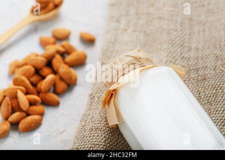 Latte di mandorle in una bottiglia con una manciata di grani e un cucchiaio di legno con un panno di tela di burlap su sfondo chiaro. Vista dall'alto Foto Stock