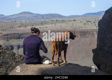 Single donna con cane si prepara a roccia in salita. Trout Creek, Oregon Foto Stock