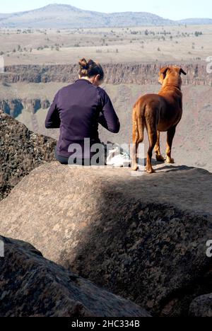 Single donna con cane si prepara a roccia in salita. Trout Creek, Oregon Foto Stock